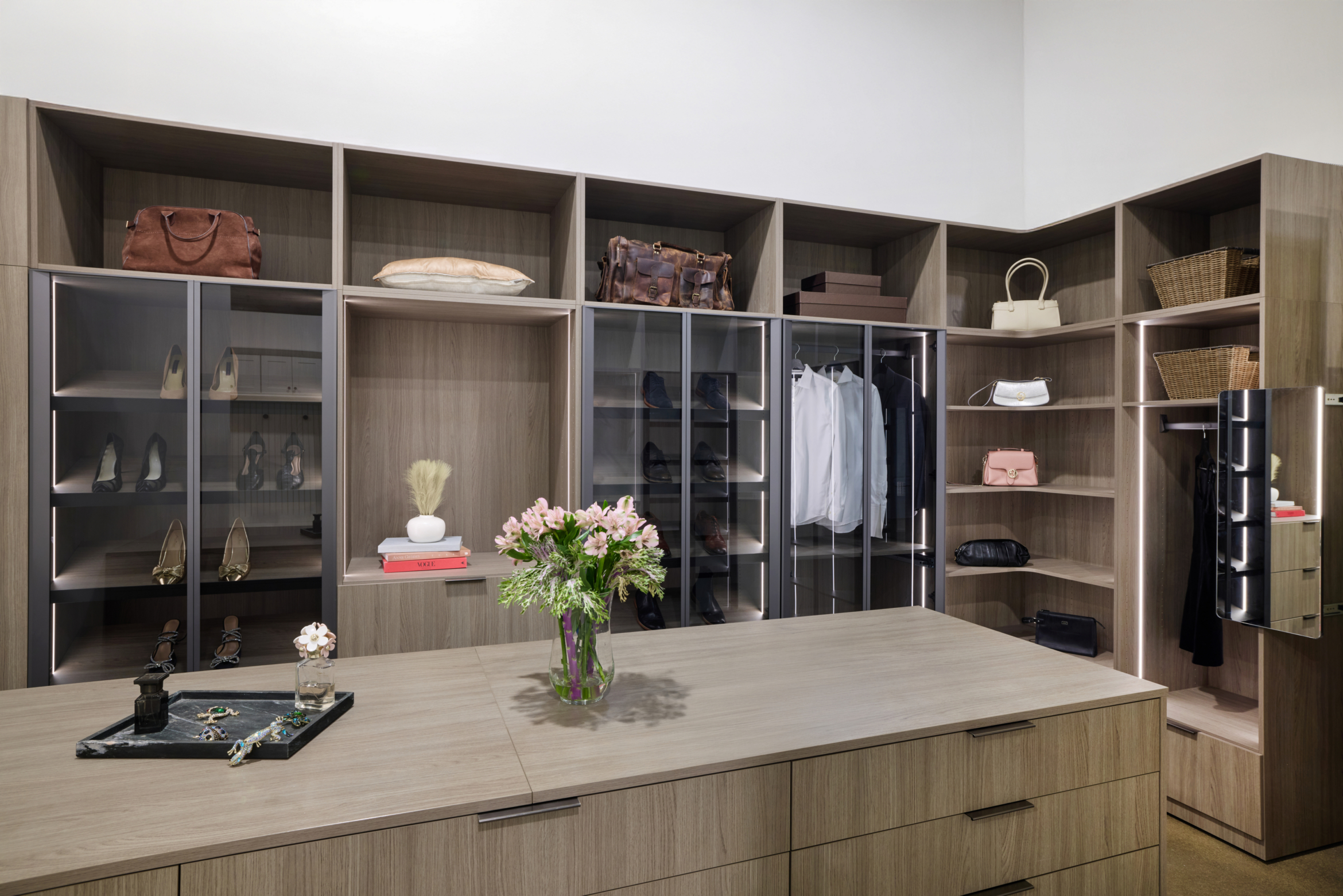 Modern custom closet featuring dark built-in cabinetry, multiple hanging sections for shirts and pants, and top-tier open shelving.