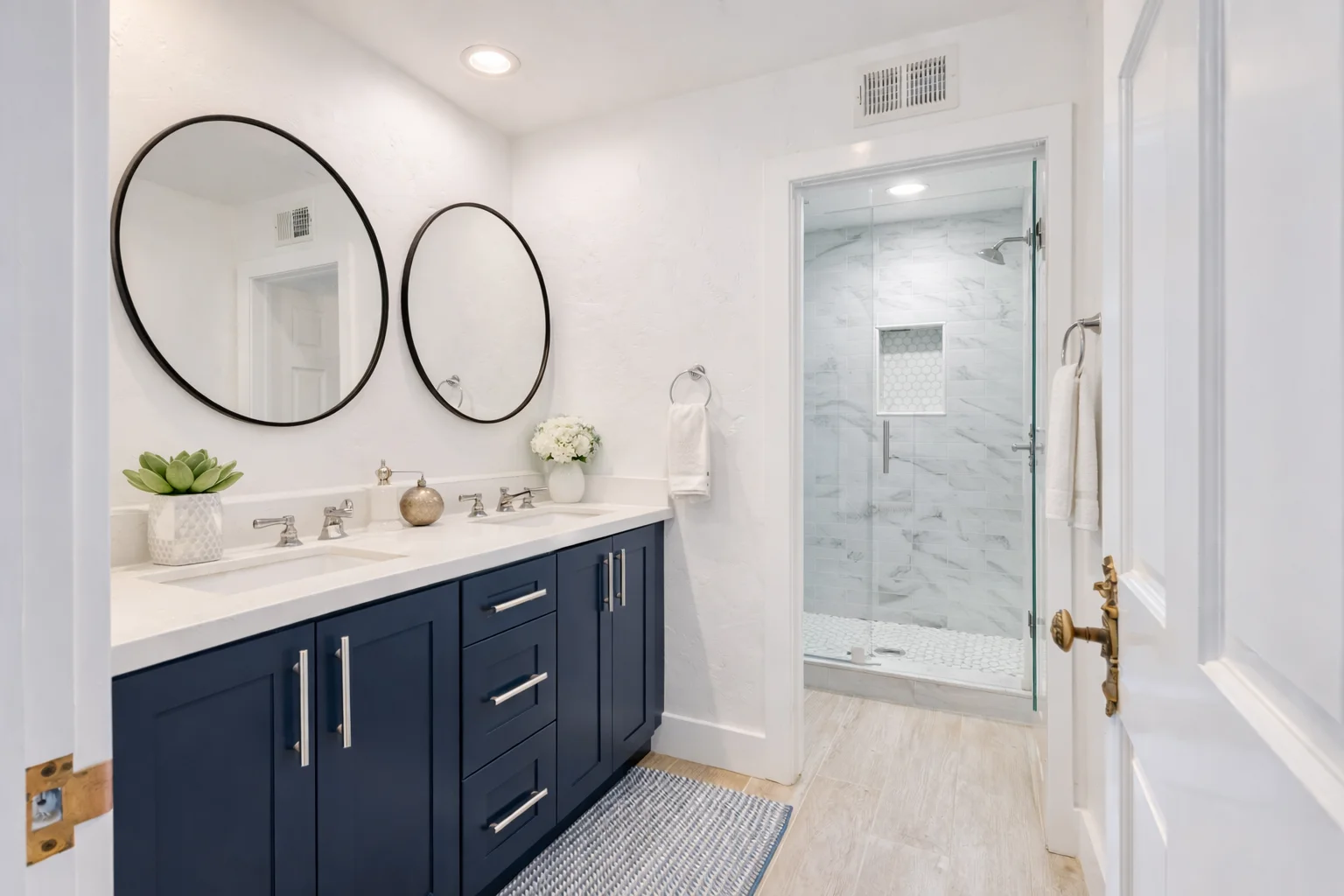 Modern bathroom featuring a custom midnight blue double vanity with an integrated makeup desk, dual round mirrors, and white countertops.