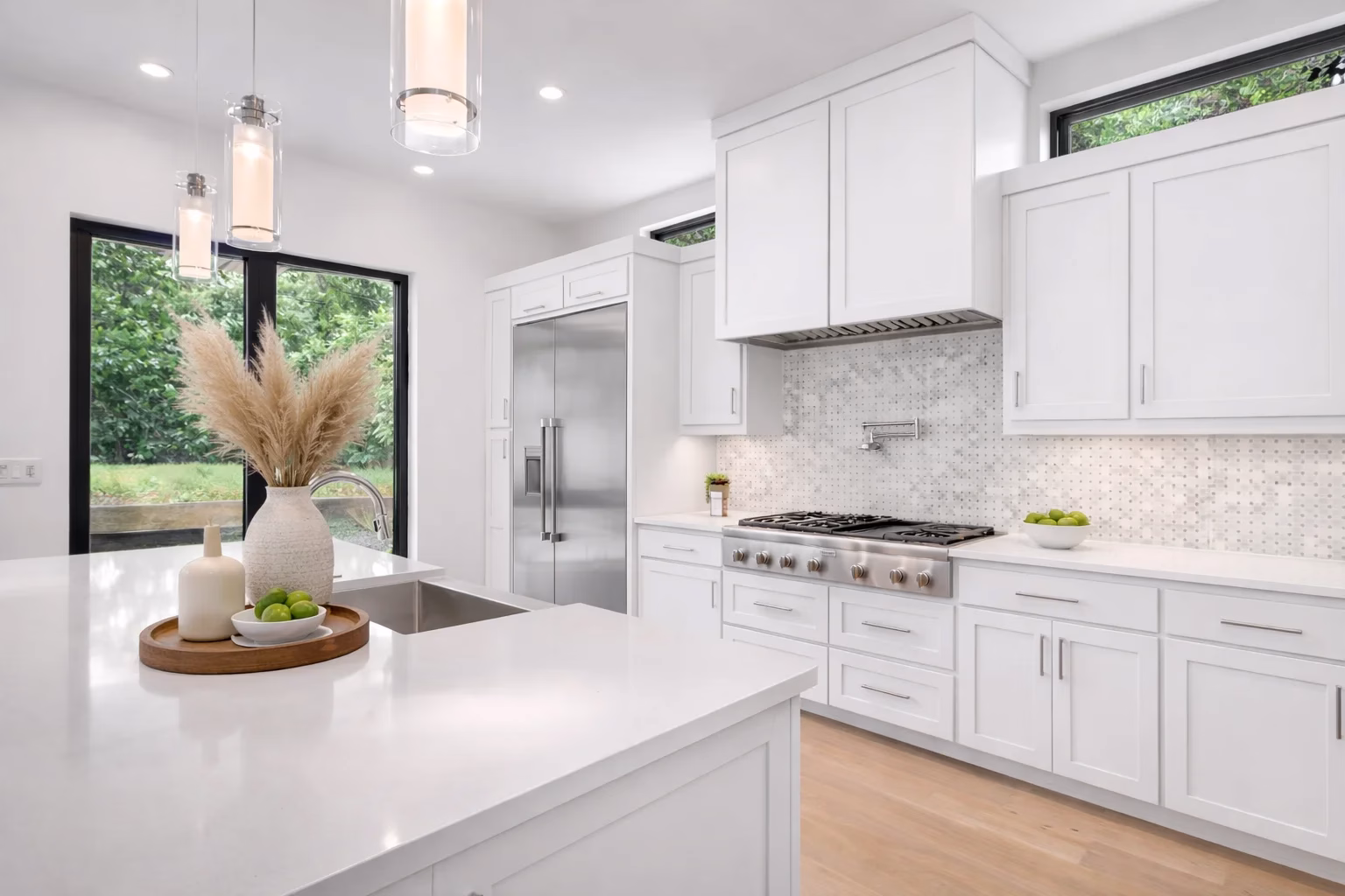 Bright kitchen featuring custom white shaker cabinets, a large island with white countertops, and pendant lighting.