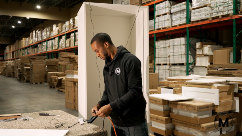 A craftsman assembling custom white closet cabinetry using power tools inside the Modernform Cabinets and Closets warehouse in Carrollton, Texas.