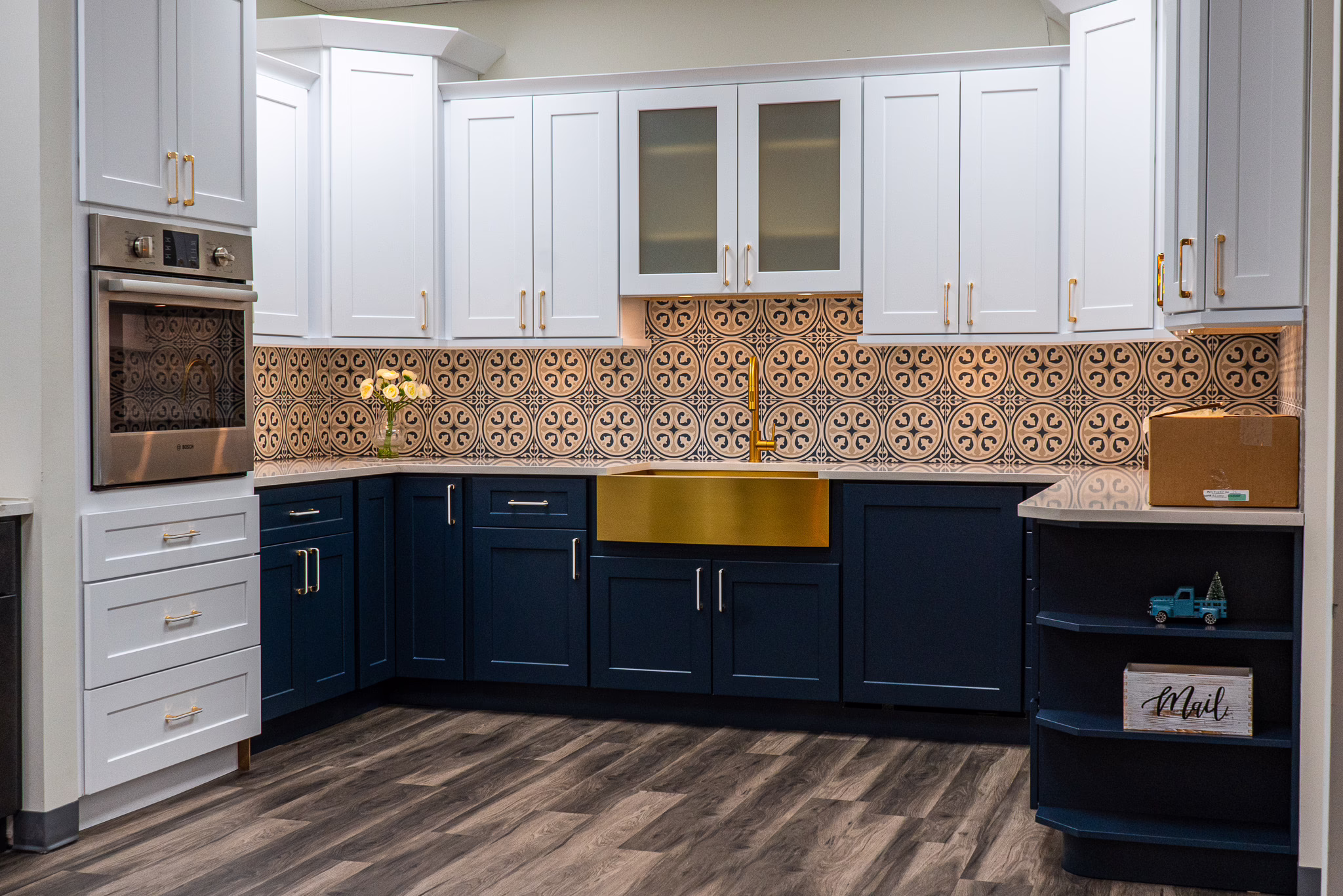 Two-tone kitchen display featuring navy blue lower shaker cabinets, white upper cabinetry, gold farmhouse sink, and patterned tile backsplash at Modernform Cabinets and Closets showroom in Carrollton Texas