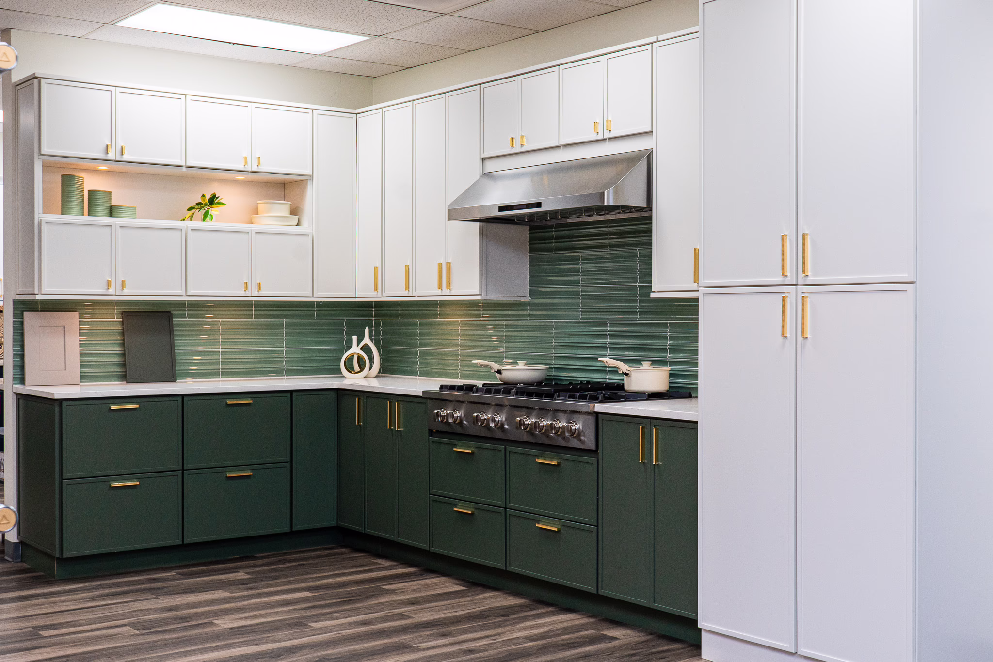age green slim shaker base cabinets with gold handles paired with white upper cabinetry, green tile backsplash, and a tall white pantry cabinet at Modernform Cabinets and Closets showroom in Carrollton Texas