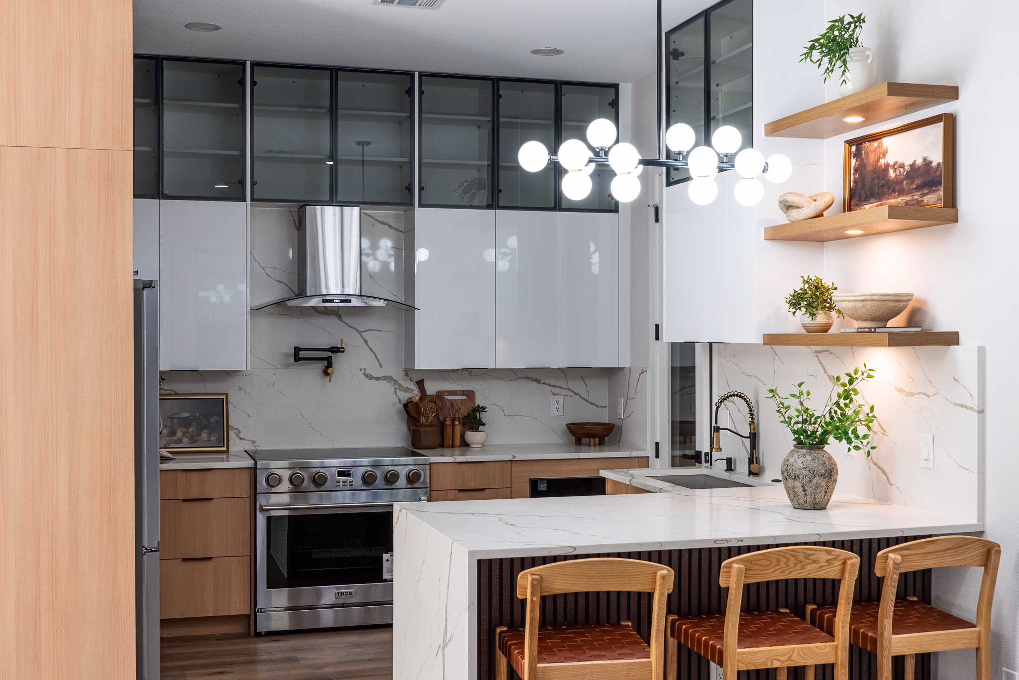Modern European frameless kitchen featuring glossy white upper cabinets, natural oak base cabinets, a quartz waterfall island with bar seating, and brass accents in a Dallas home.