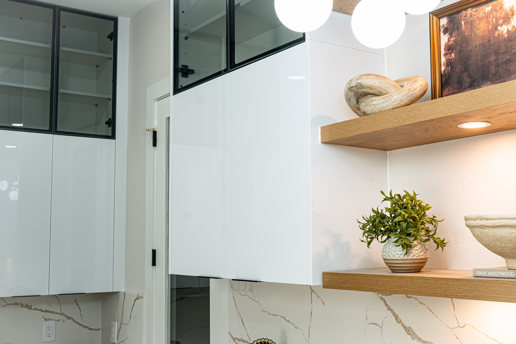 Modern white upper cabinets and natural oak base cabinets with brass hardware, open wood floating shelves, and a marble-look backsplash in a Dallas home.