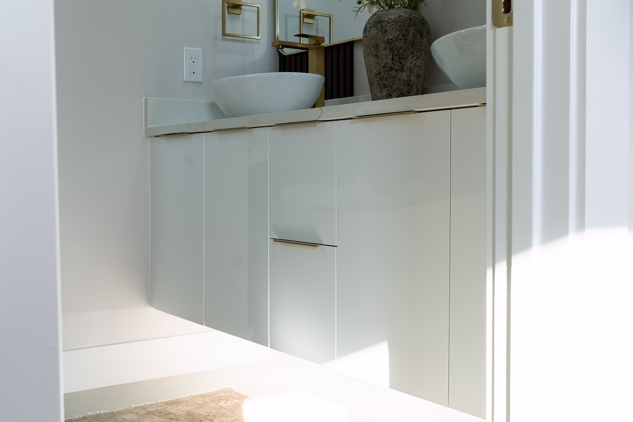 Modern glossy white European frameless floating double vanity with integrated vessel sinks, wall-mounted brass faucets, and twin rectangular mirrors in a Dallas home.