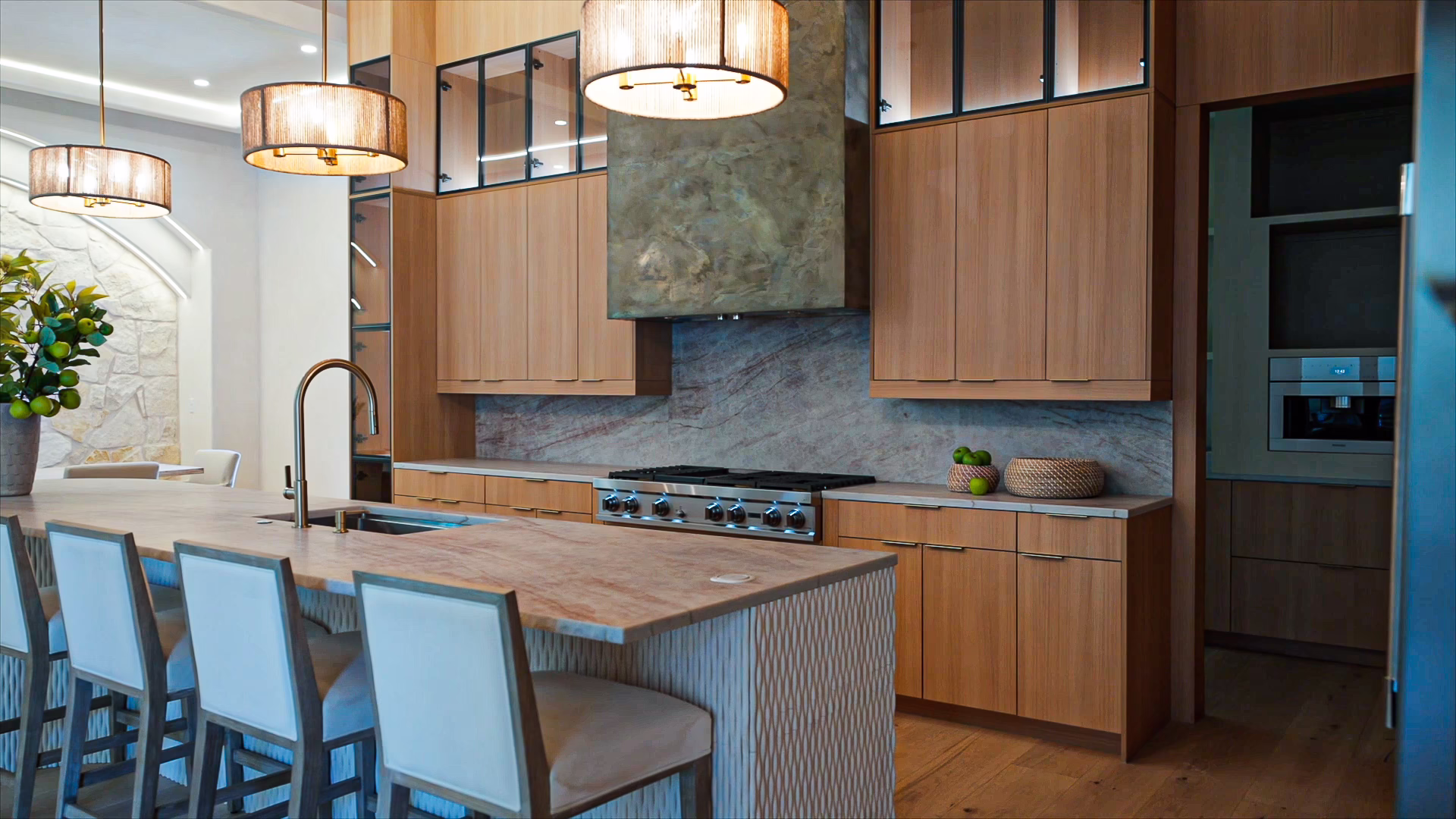 Natural oak European frameless kitchen featuring a wood island with a fluted waterfall base, leather dining chairs, pendant light fixtures, and matching oak cabinetry with integrated appliances.