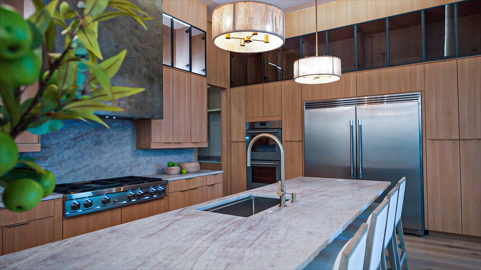 Modern natural oak European frameless kitchen featuring a marble waterfall island with barstool seating, integrated stainless steel appliances, and pendant lighting.