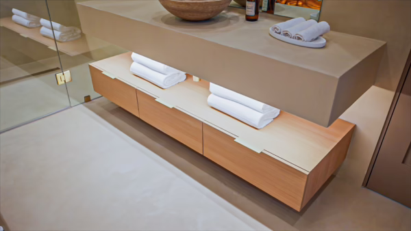 Modern natural oak European frameless floating bathroom vanity with handleless pull drawers and white folded towels under a stone floating counter.